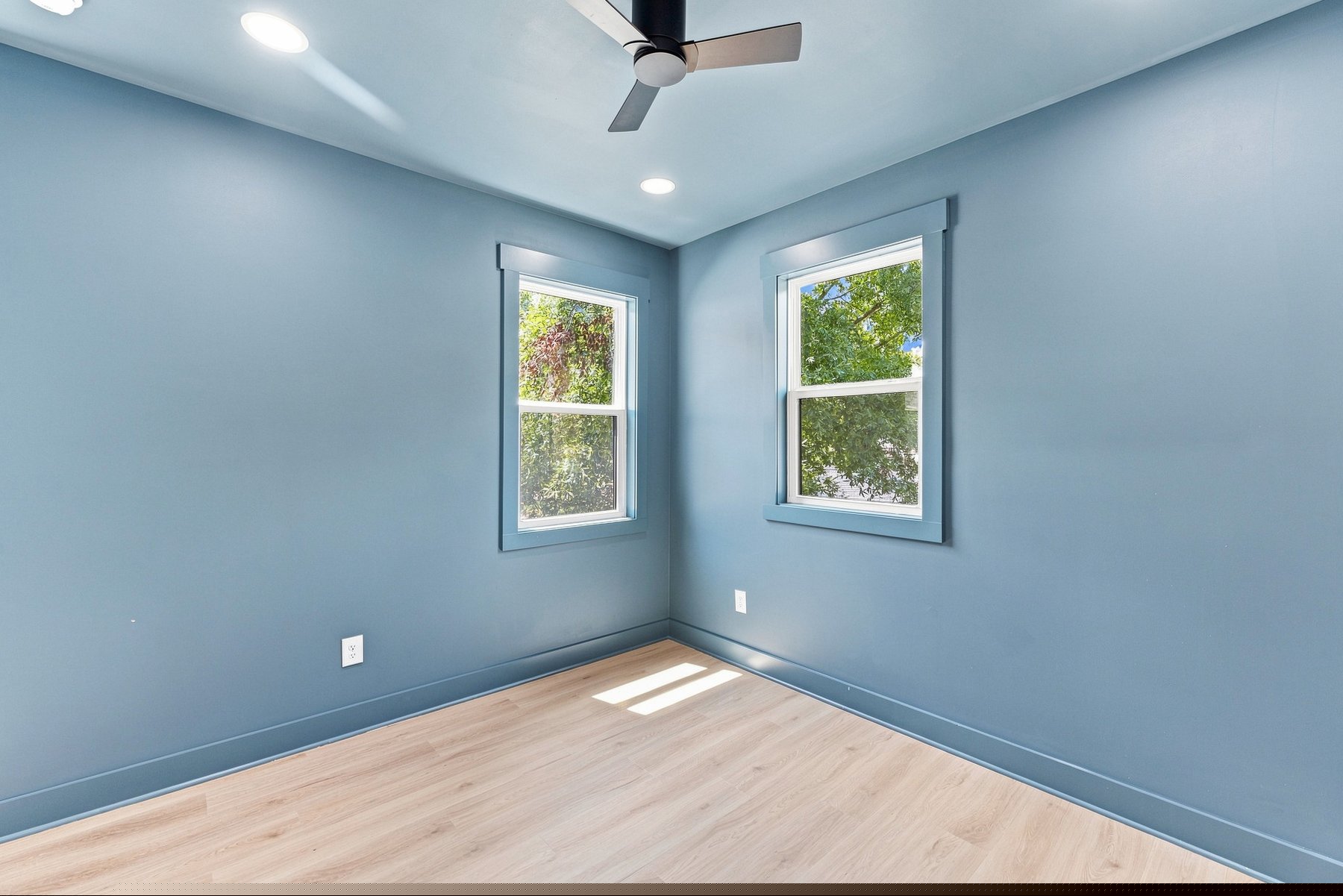One-bedroom loft bedroom with two windows, blue accent wall, ceiling fan, and warm wood floors