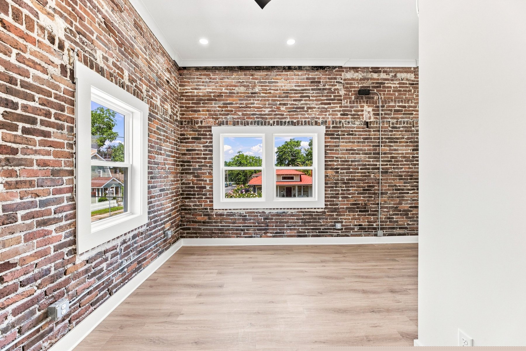 Bright loft room with preserved exposed brick, tall windows, a ceiling fan, and warm wood floors