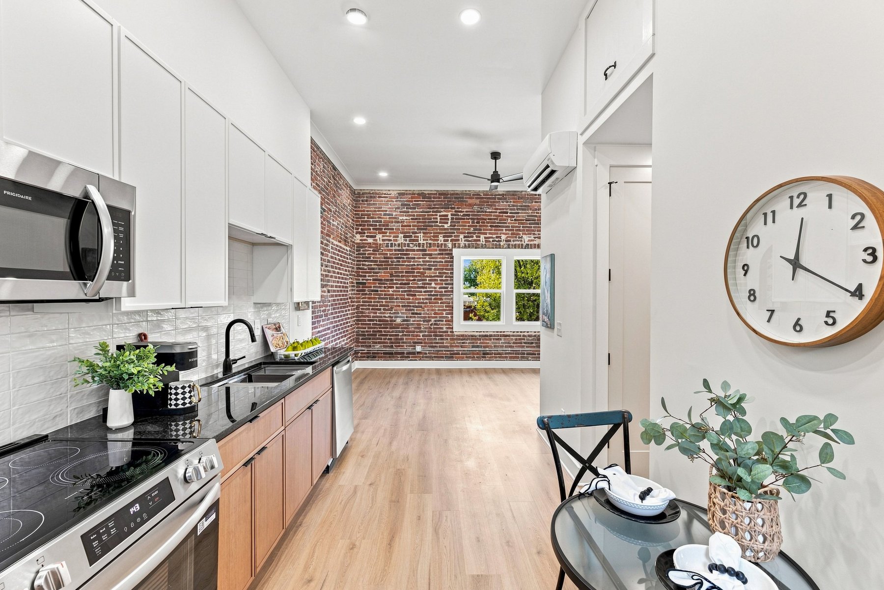 Finished loft kitchen opening into the living area with exposed brick, warm wood cabinetry, and black fixtures