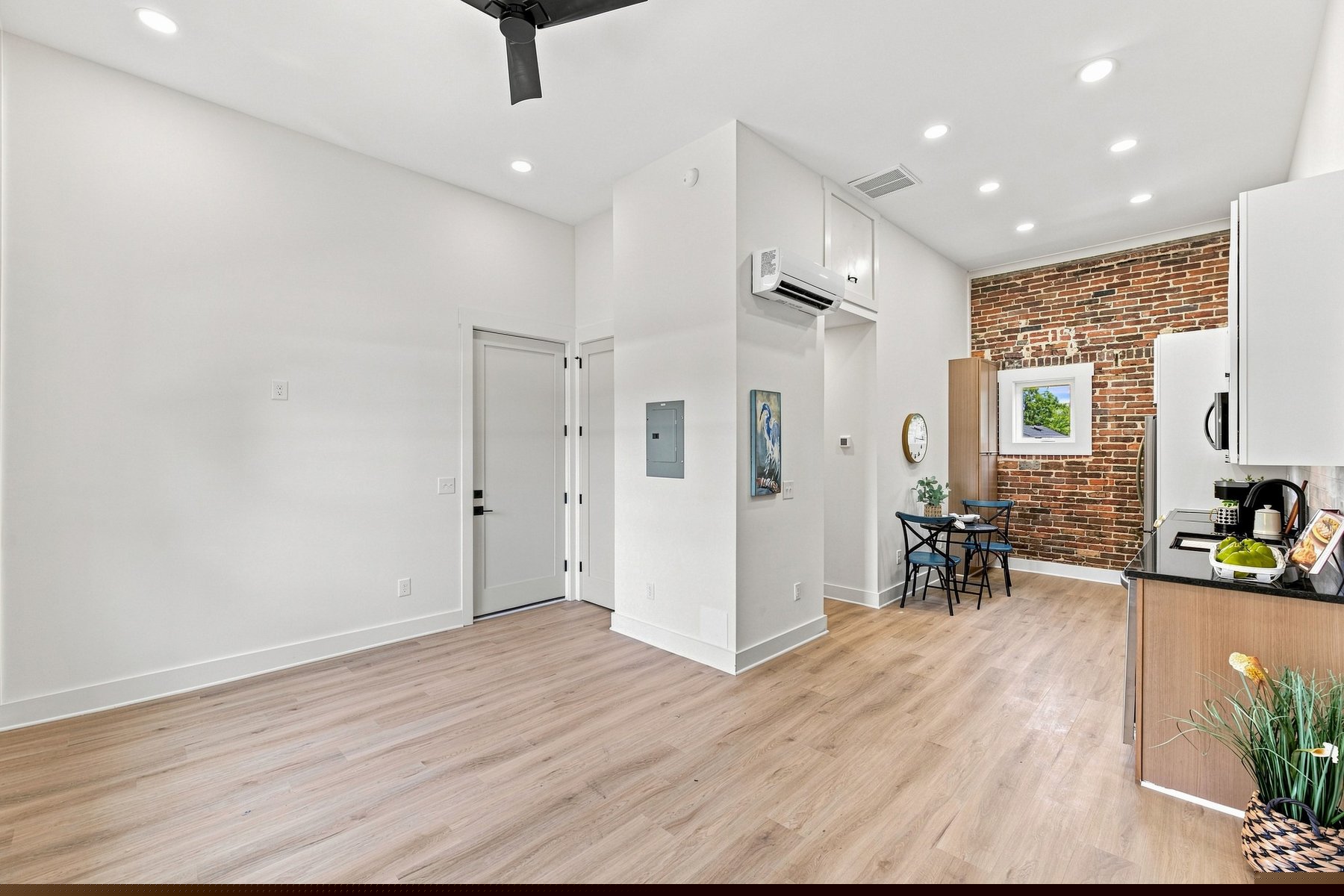 Open one-bedroom loft with exposed brick, tall windows, kitchen, dining area, and warm wood floors